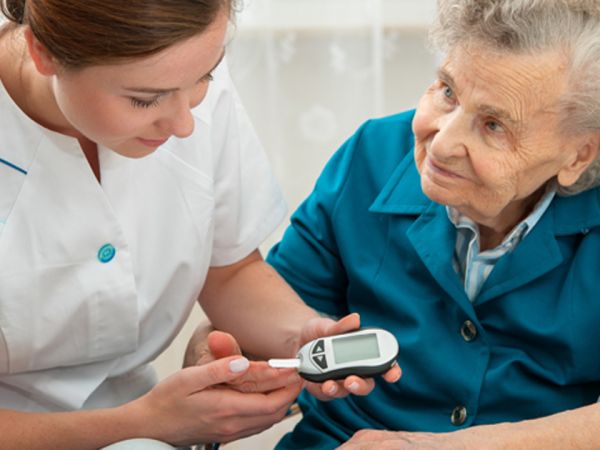 Female nurse measuring blood glucose level of senior woman